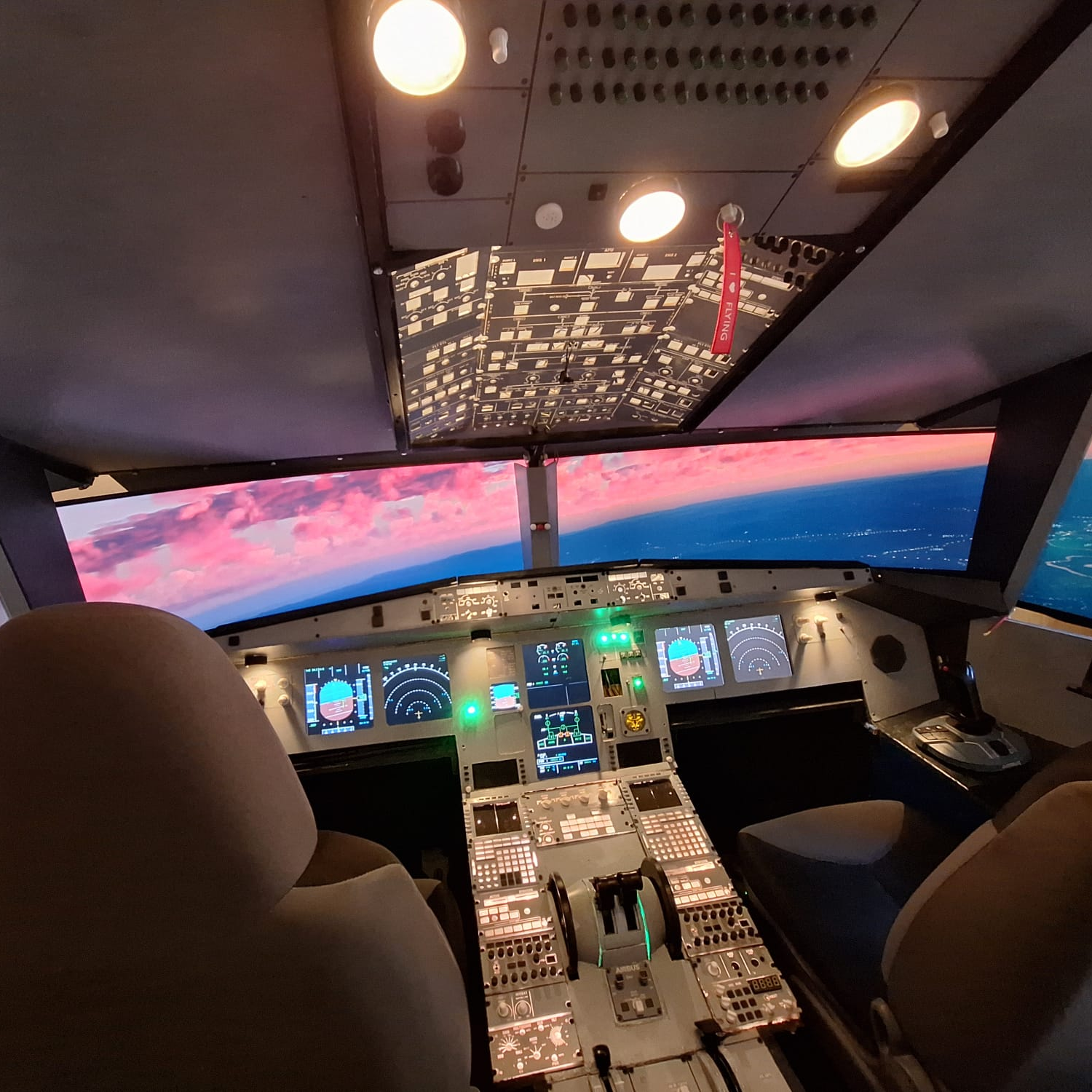 Innenansicht eines Airbus‑A320neo-Flugsimulators mit beleuchtetem Cockpit und Blick auf einen farbenfrohen Sonnenuntergang.