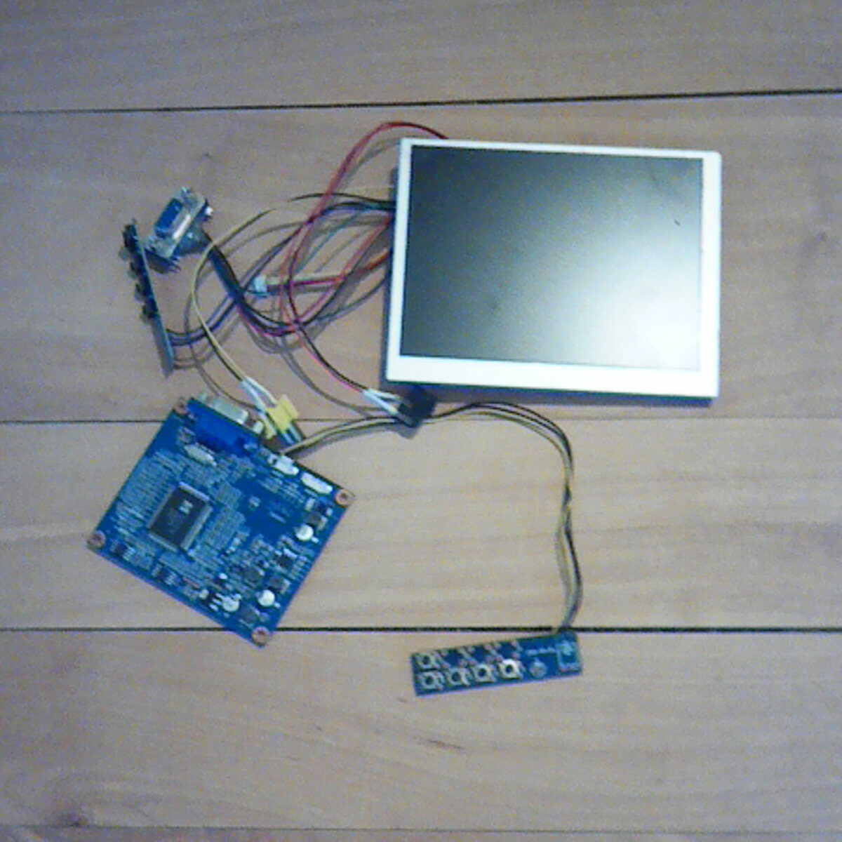 Auf einem Holztisch liegendes LCD‑Panel mit verbundenen Platinen und Kabeln.