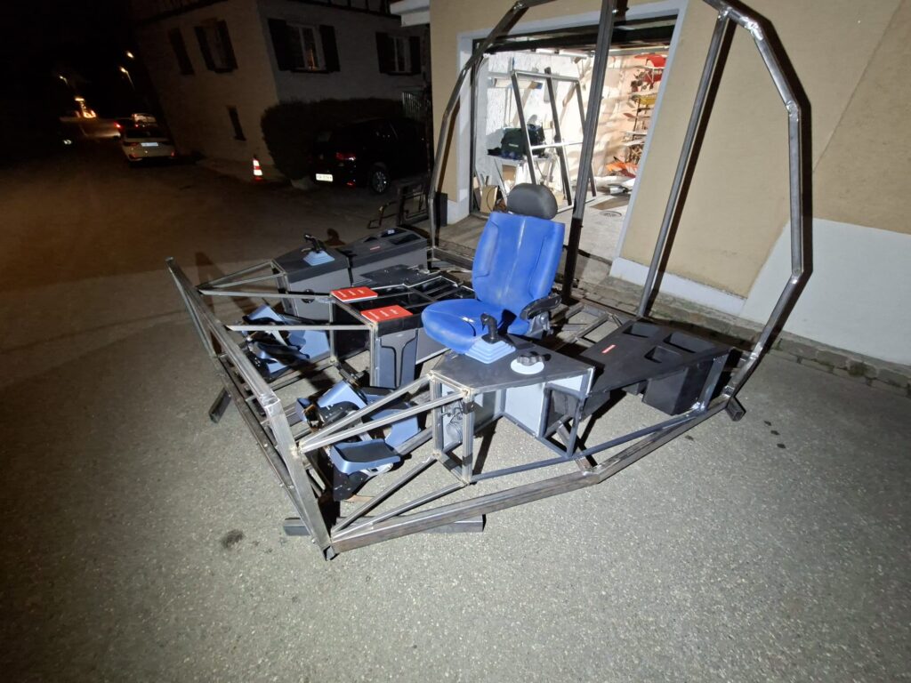 Flugsimulator-Rahmen mit blauem Sitz im Freien bei Nacht während der Bauphase.